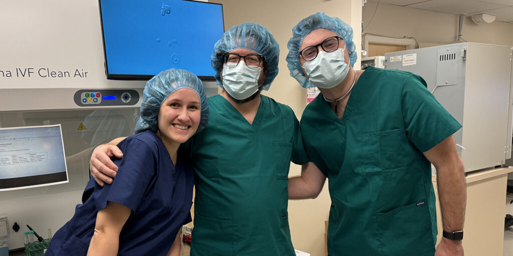 Project team members Savana Biondic, Dr. Jeremy Grushcow and Dr. G. Adam Reeves in front of a microscope image of a research-donated embryo