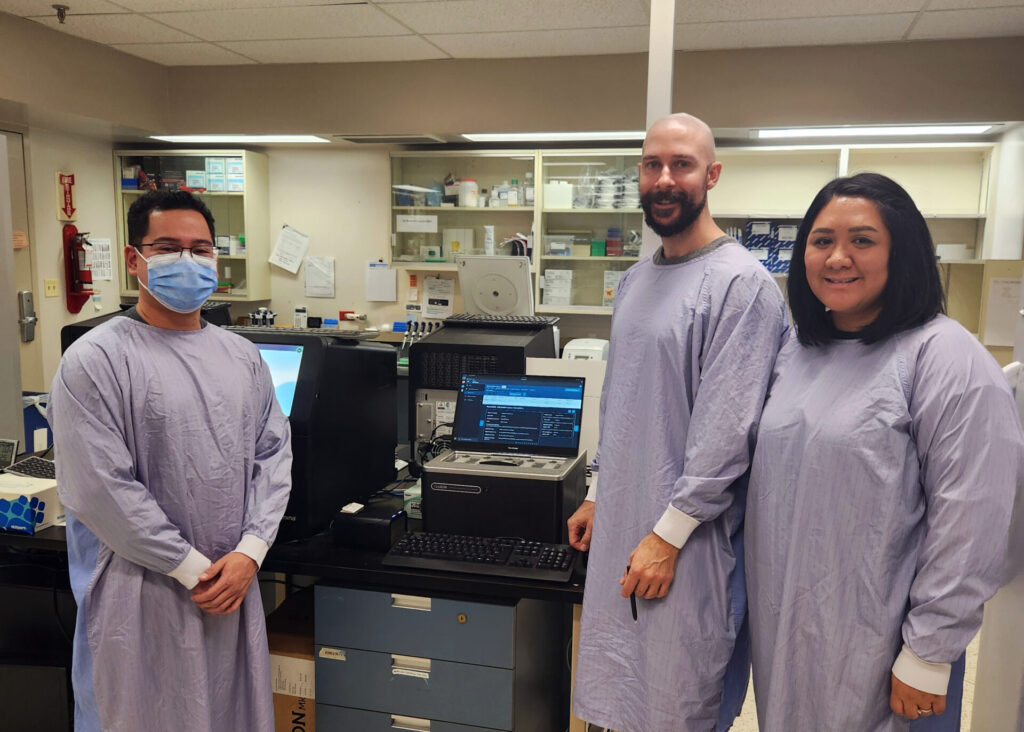 Lab technicians Vince Benedicto, Brendan McKenzie and Edlyn Dunlop by the Oxford Nanopore GridIon.