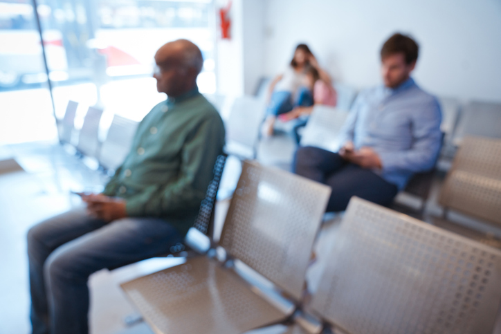 Defocused image of people at waiting room. Patients are waiting at hospital. They are sitting on seat.